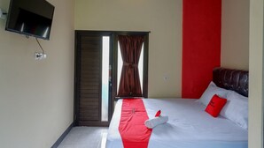 A hotel room with a bed, a TV mounted on the wall, and a door with curtains. - RedDoorz @ Gerbang Dieng Plateau Area (Kejajar)