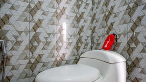 A toilet with a red bidet attachment in a bathroom with patterned tile walls. - RedDoorz @ Gerbang Dieng Plateau Area (Kejajar)