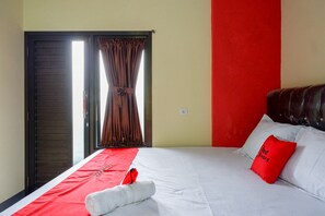 Een hotelkamer met een bed, een rode en witte dekbedovertrek, een rood kussen en een raam met gordijnen.