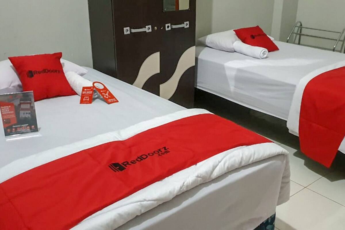 Zwei Hotelbetten mit roter und weißer Bettwäsche, ein RedDoorz-Schild und eine Broschüre auf dem Bett links.