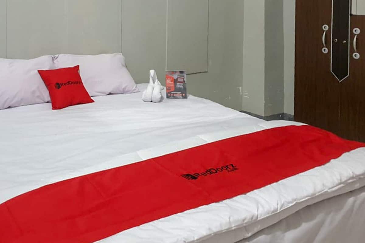 Ein Hotelzimmer mit einem Bett, einer roten und weißen Bettdecke, einem roten Kissen und einem weißen, schwanenförmigen Kissen.