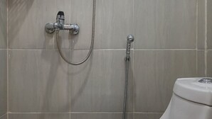 Un baño con inodoro, ducha con cabezal de ducha manual y grifo empotrado.