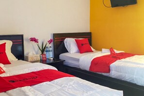 Habitación de hotel con dos camas, cada una con ropa de cama blanca y detalles en rojo, una mesita de noche con un jarrón de flores y un televisor montado en la pared.