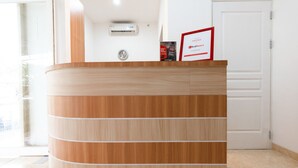 A reception desk with a wooden finish, a clock, and a framed sign on top. - RedDoorz @ Graha Cemerlang Maros (Mandai)