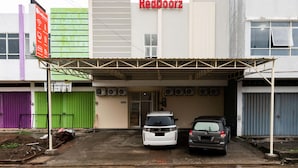 A RedDoorz building with a covered parking area, two cars parked, and a green and purple gate. - RedDoorz @ Graha Cemerlang Maros (Mandai)