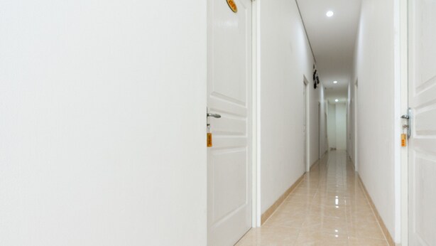 A long, narrow hallway with white walls and a shiny tiled floor. - RedDoorz @ Graha Cemerlang Maros (Mandai)