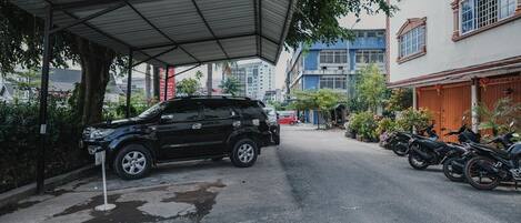 Un SUV negro estacionado bajo una estructura cubierta, con un árbol cerca.