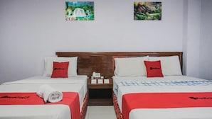Une chambre d’hôtel avec deux lits, chacun recouvert d’une courtepointe rouge et blanche, dotée d’une tête de lit en bois et d’une table de chevet avec un téléphone et un bloc-notes.