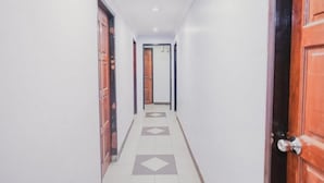 Un couloir étroit, avec des portes en bois de chaque côté et un sol carrelé orné d’un motif géométrique.
