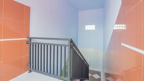 Una escalera con barandilla de metal, paredes de azulejos naranja y blancos, y un ventanal en la parte superior.