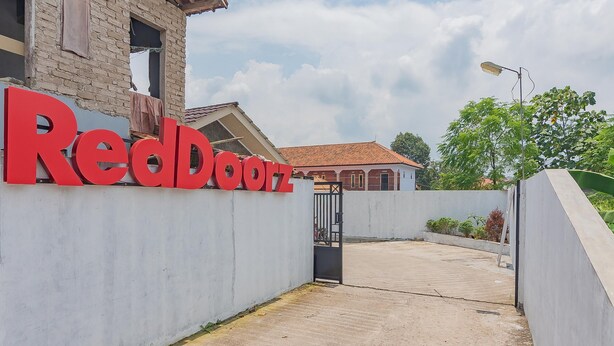 Un letrero de RedDoorz, una entrada con portón y un edificio con techo de tejas.