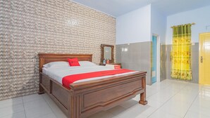Una habitación de hotel con una cama de madera, un espejo, un almohadón rojo y una cortina amarilla.