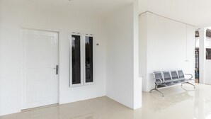 Passadís ampli i ben il·luminat amb una porta blanca, una banca i una porta doble amb panells de vidre.