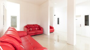 Un ampli saló modern amb un sofà seccional vermell gran i un sofà vermell més petit. L'espai presenta un disseny minimalista amb parets blanques i un terra de rajola.
