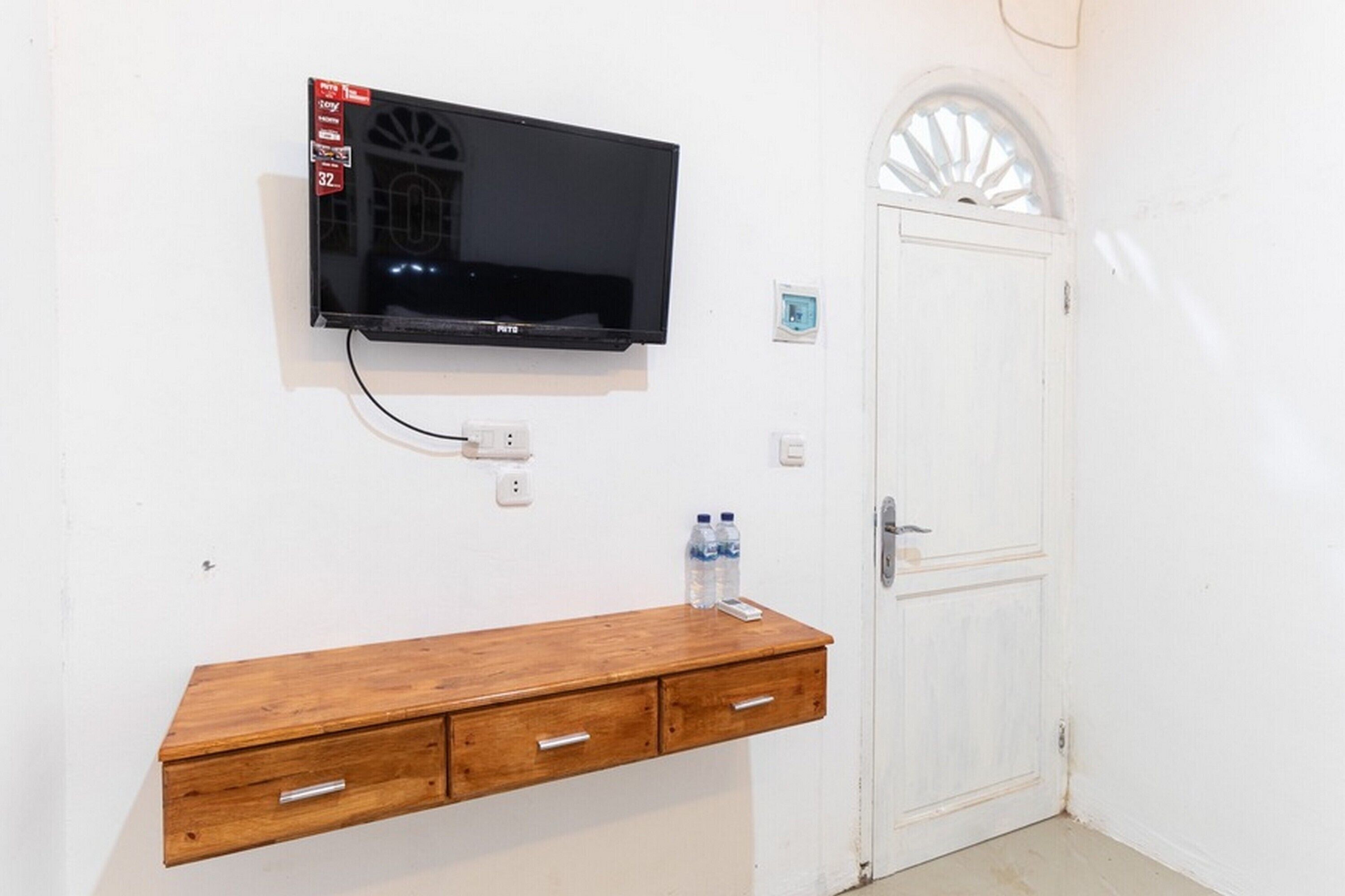 A room with a mounted TV, a wooden cabinet, and a white door.
