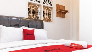 Habitació d'hotel amb un llit, roba de llit blanca, una manta vermella i el logotip de RedDoorz a les almoinades i una tovallola.