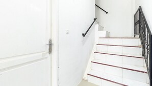 Una porta blanca amb el número 109, una escala de graons blancs i detalls vermells, i una barana metàl·lica negra.