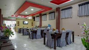 Un área de comedor con varias mesas y sillas, un televisor montado en la pared y un mostrador de recepción al fondo.