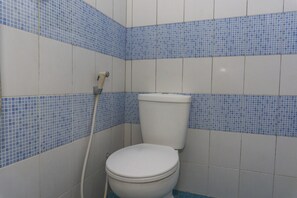 Une salle de bain avec des toilettes, des murs carrelés de bleu et de blanc, et une tuyauterie apparente.