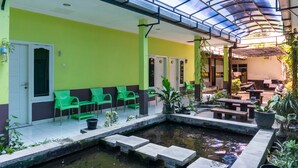 A covered outdoor area with green chairs, a small pond, and a seating area with tables and benches.