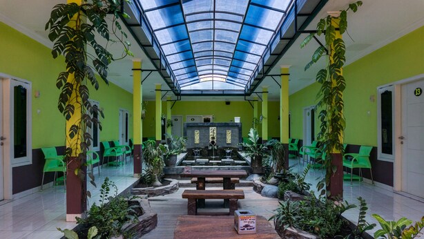 A spacious indoor area with a skylight, green walls, and multiple seating areas with plants.