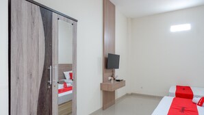 Ein Hotelzimmer mit einem Holzschrank, einem an einer Holzplatte montierten Flachbildfernseher, zwei Betten mit roten Bettdecken und einem kleinen Nachttisch.