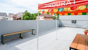 Eine Dachterrasse mit rotem Sonnensegel, das 'PROURAT' zeigt, einer Holzbank und einem Tisch mit Blumentöpfen.