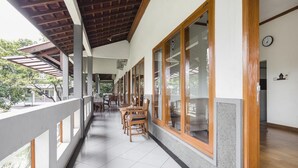 A covered outdoor area with a long table and chairs, large windows, and a wooden ceiling. - RedDoorz Plus @ Purwodadi (Lawang)