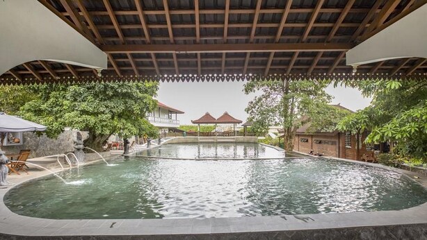 A pool area with a covered seating area and a gazebo in the background. - RedDoorz Plus @ Purwodadi (Lawang)