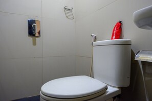 Un bany estàndard amb un vàter blanc, un assecador de mans i una bossa vermella penjada a la paret.