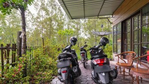 Un espace extérieur abrité, avec deux motos garées sur un sol carrelé en forme d’hexagone, entouré de verdure et d’une clôture en bois.