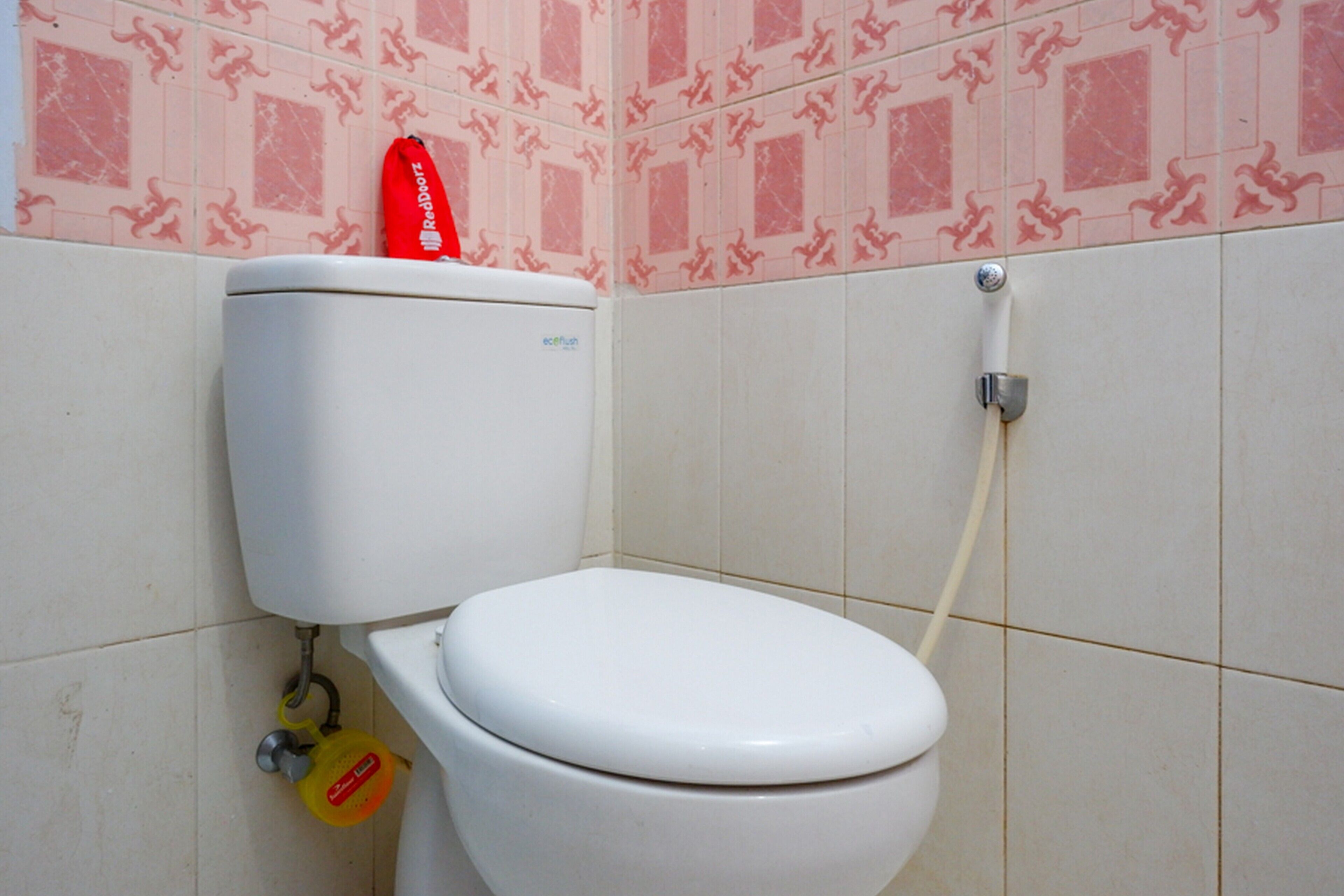 A white toilet with a red tissue box on top, a yellow toilet paper holder, and a toilet paper roll.