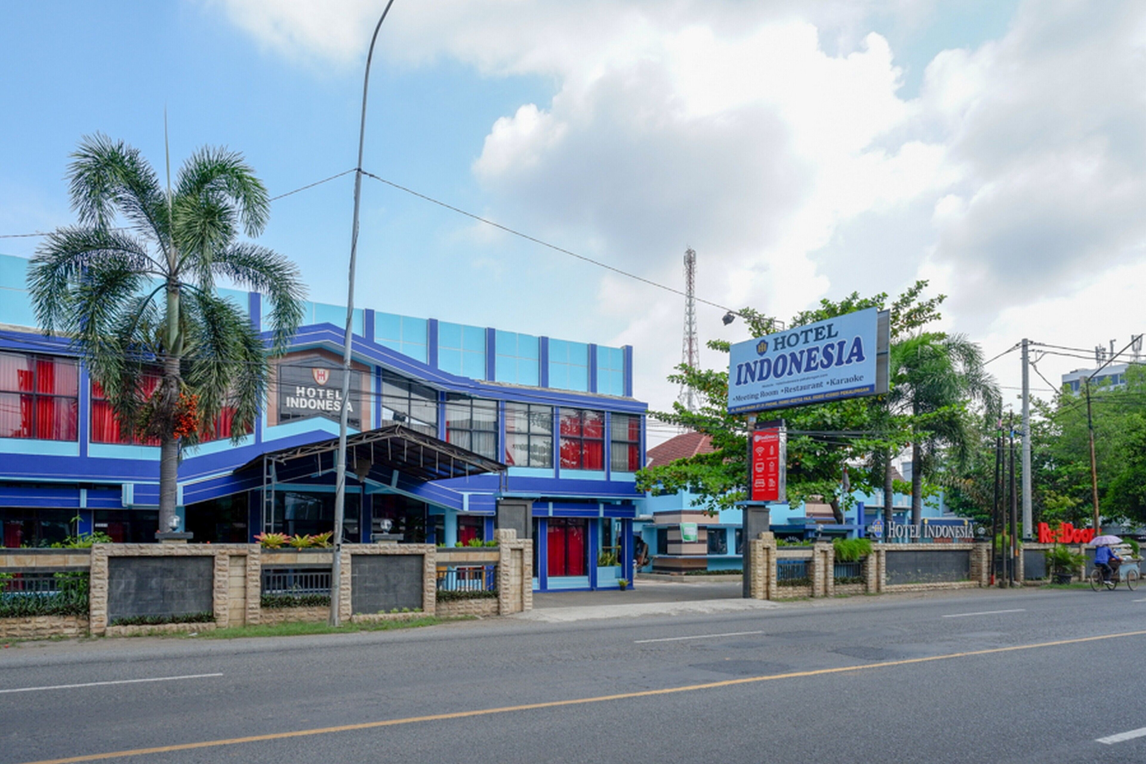 A hotel with a blue facade, palm trees, and a sign that reads "Hotel Indonesia".