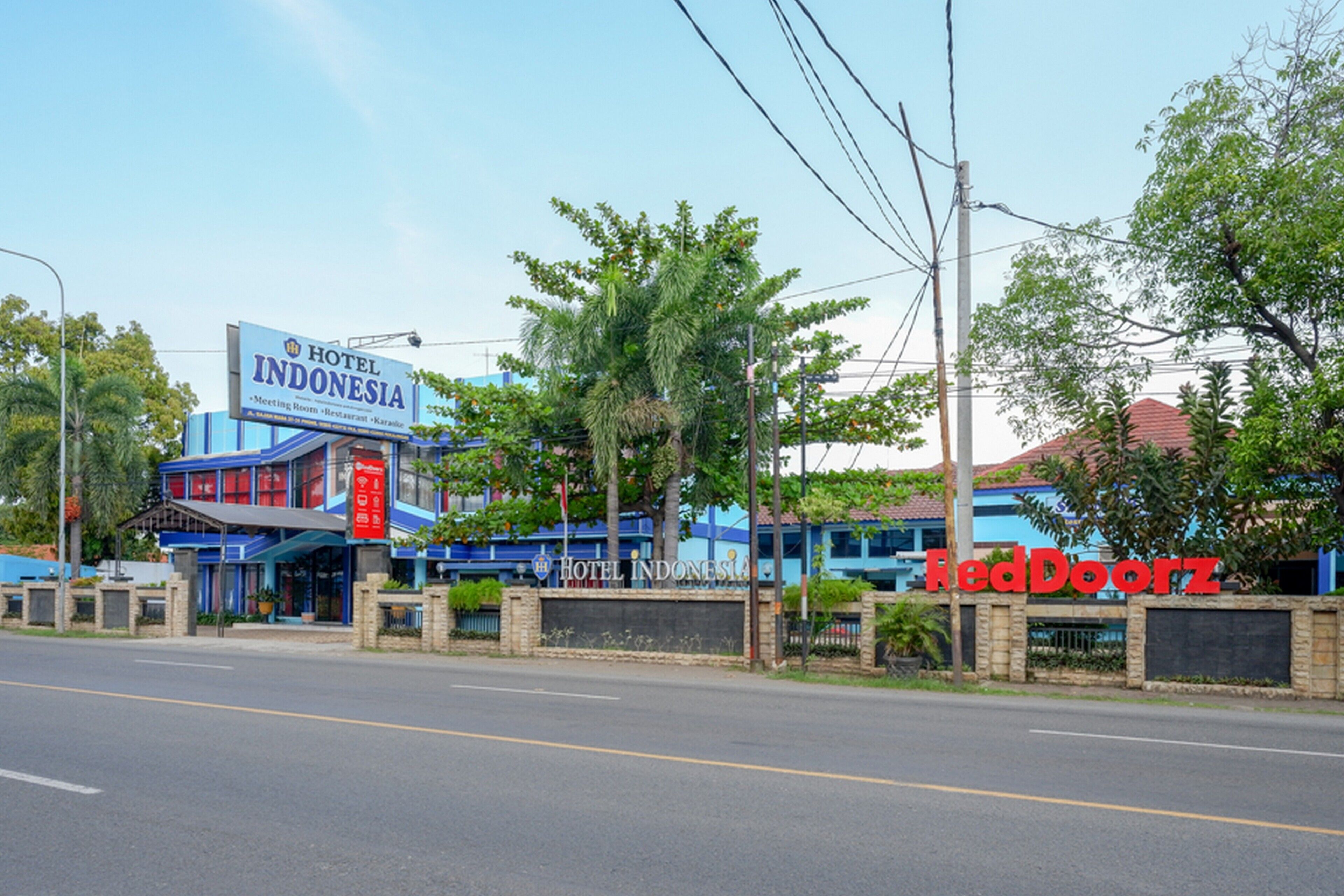 Um hotel chamado 'Hotel Indonesia' com uma placa, o logotipo RedDoorz e uma estrada visível à frente.