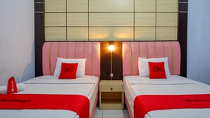 Ein Hotelzimmer mit zwei Betten, jeweils mit roter Bettdecke und Kissen, einem hölzernen Nachttisch und einer Wandleuchte.