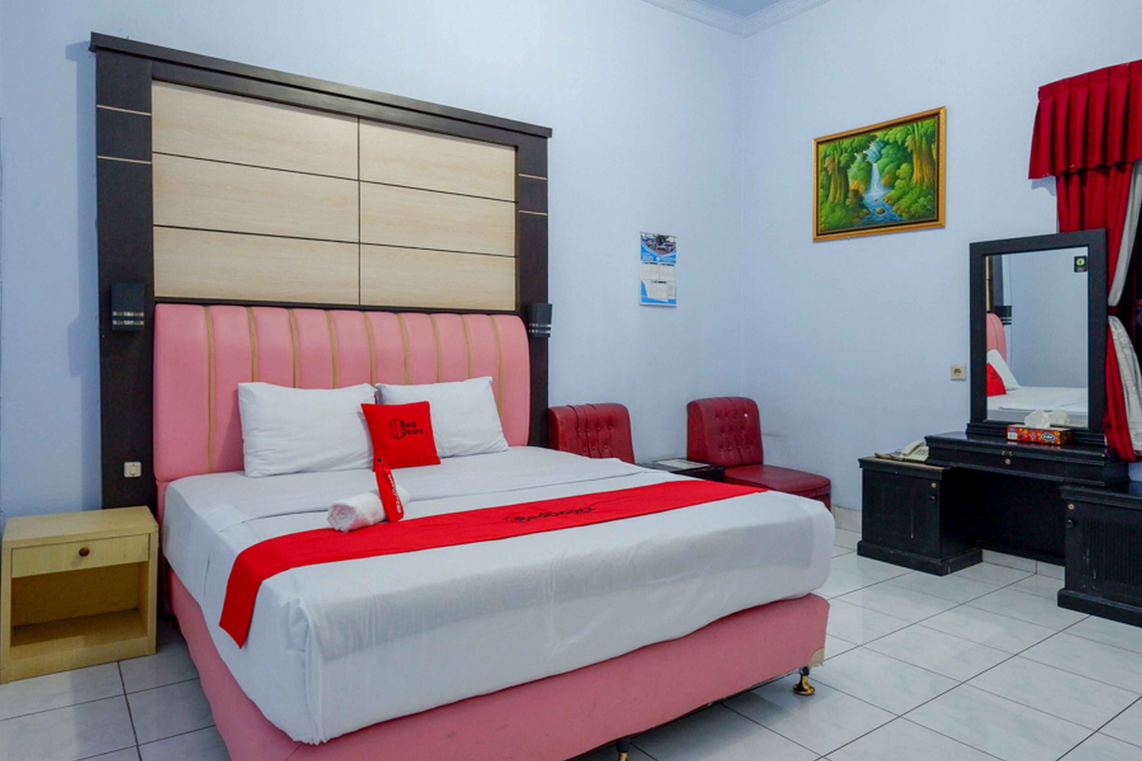 A neatly arranged bedroom with a large bed, a bedside table, a chair, a desk, and a mirror.