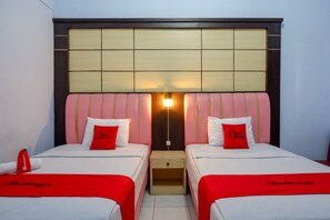 A hotel room with two beds, each with a red blanket and matching pillows, a wooden headboard, and a nightstand between the beds.