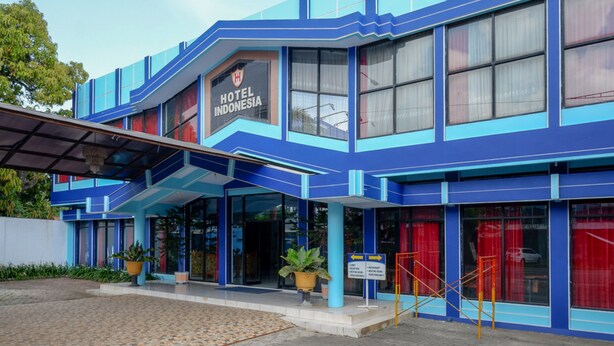 Ein modernes Hotel mit blauer Fassade, einem gut sichtbaren Schild mit der Aufschrift 'HOTEL INDONESIA' und einem überdachten Eingangsbereich.