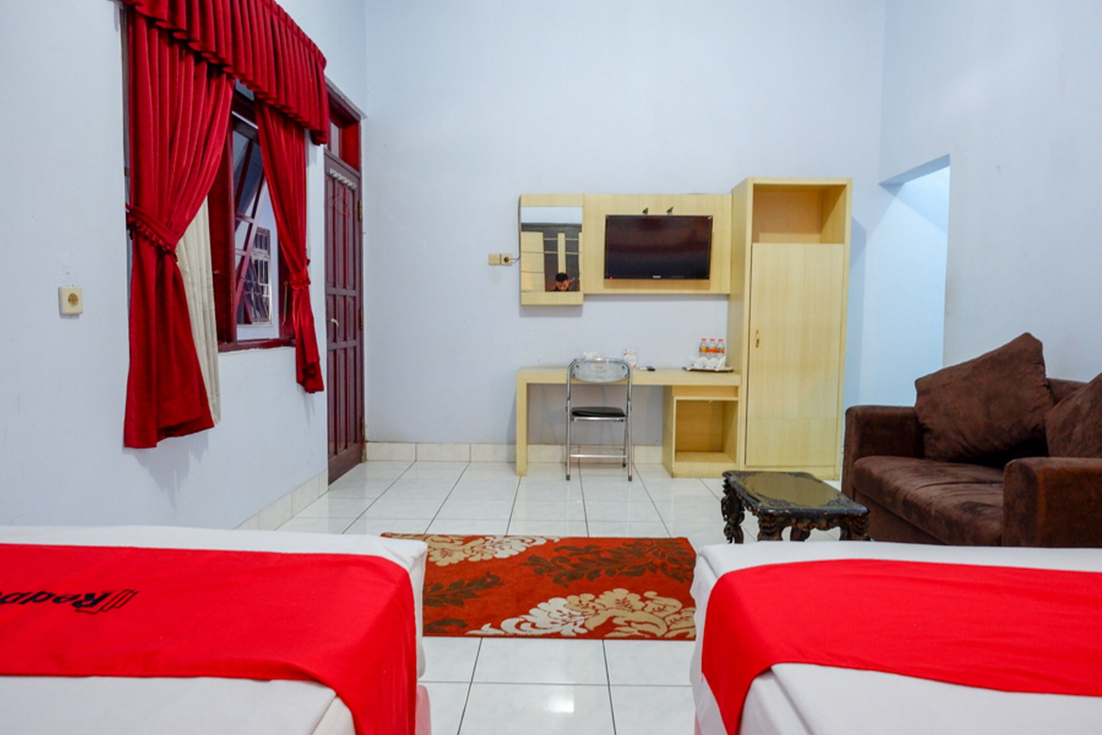 A room with two beds, a desk with a chair, a television, and a wardrobe.