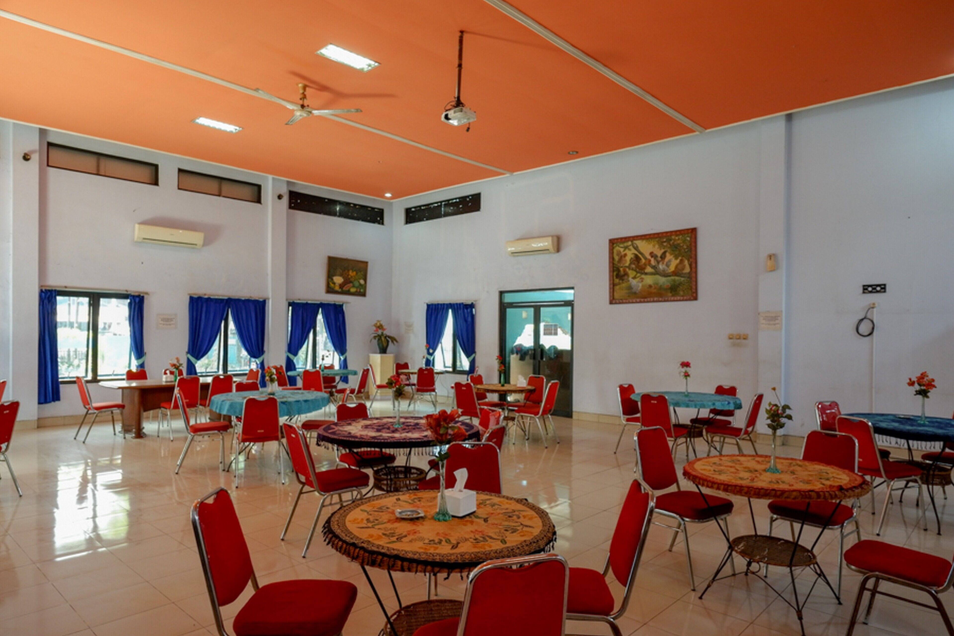 A spacious dining hall with high ceilings, red chairs, and round tables.