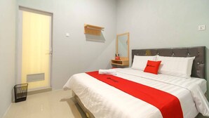 A neatly made bed with a red and white bedspread, a bedside table with a lamp, and a mirror on the wall.
