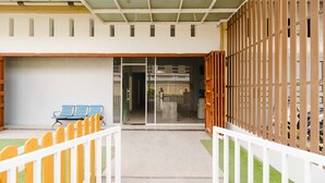 A building entrance with a glass door, a white fence, and blue chairs outside.