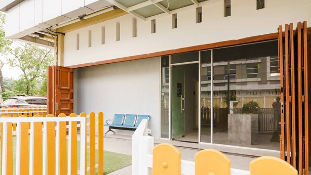 A modern building with a glass entrance, a wooden fence, and blue chairs outside.