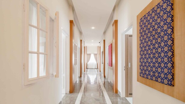 A long, narrow hallway with a shiny floor, white walls, and wooden doors. - RedDoorz Plus Syariah @ Jalan Dr Sutomo Padang (Padang)