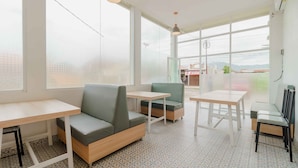 A modern indoor seating area with tables and cushioned seating, large windows with a view, and patterned flooring. - RedDoorz Plus Syariah @ Jalan Dr Sutomo Padang (Padang)