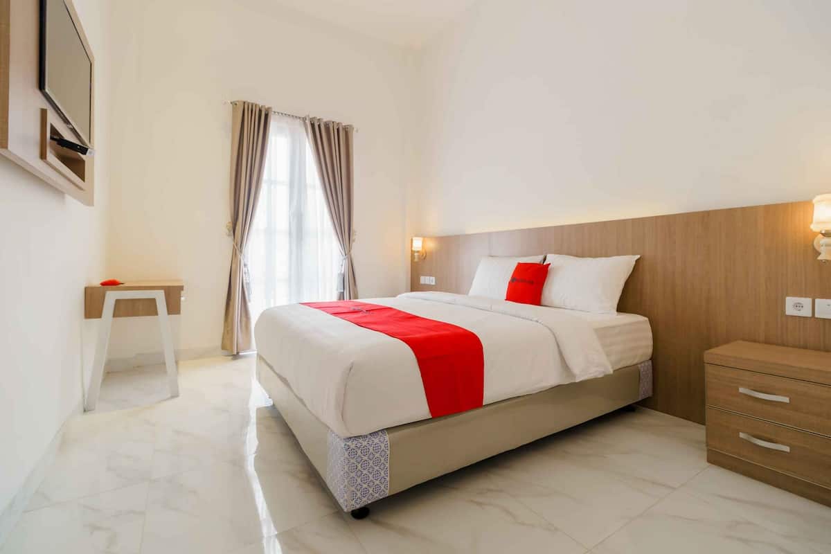 A hotel room with a bed, bedside table, and a TV mounted on the wall.