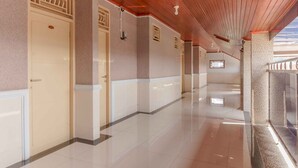A long, polished hallway with cream-colored doors and a tiled floor, leading to a balcony with a railing. - RedDoorz Plus Syariah near RSUP Dr. M. Djamil Padang (Padang)