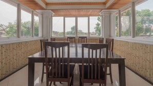 A dining area with a large table and chairs, large windows, and a wooden ceiling. - RedDoorz Plus Syariah near RSUP Dr. M. Djamil Padang (Padang)
