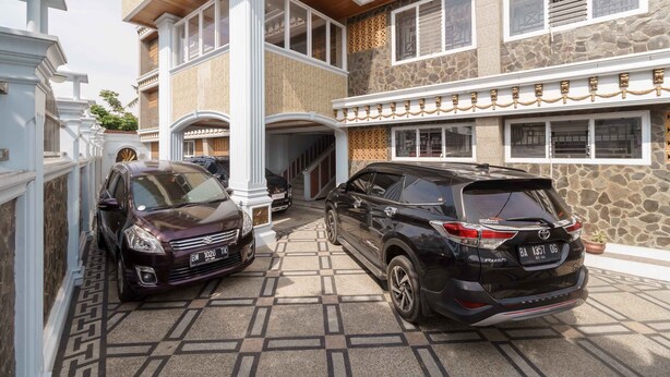A multi-story building with a stone facade, a covered entrance, and a parking area with two cars. - RedDoorz Plus Syariah near RSUP Dr. M. Djamil Padang (Padang)