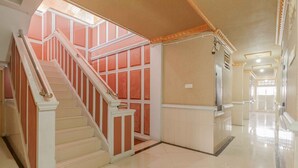 A spacious hallway with a staircase leading to a landing. The walls are adorned with decorative panels, and the floor is tiled. - RedDoorz Plus Syariah near RSUP Dr. M. Djamil Padang (Padang)